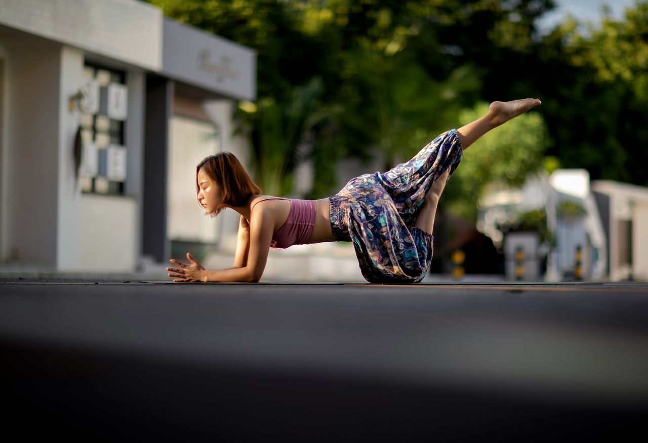 class-01 Focused Asian woman doing yoga pose outdoors on an urban street with blurred background.