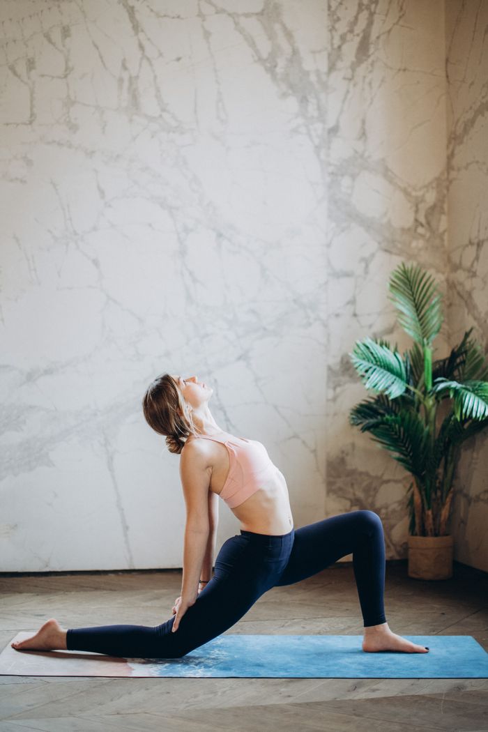 Woman practicing a deep yoga stretch indoors on a mat, promoting wellness and mindfulness.