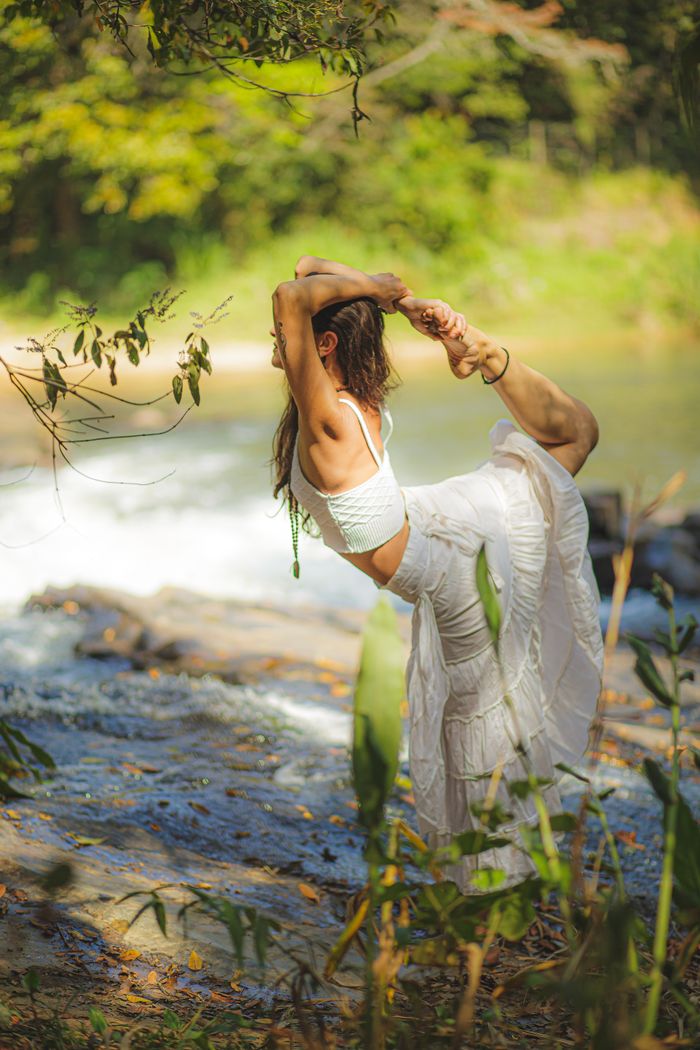 Caucasian woman demonstrating flexibility and balance in a yoga pose by a river in nature.